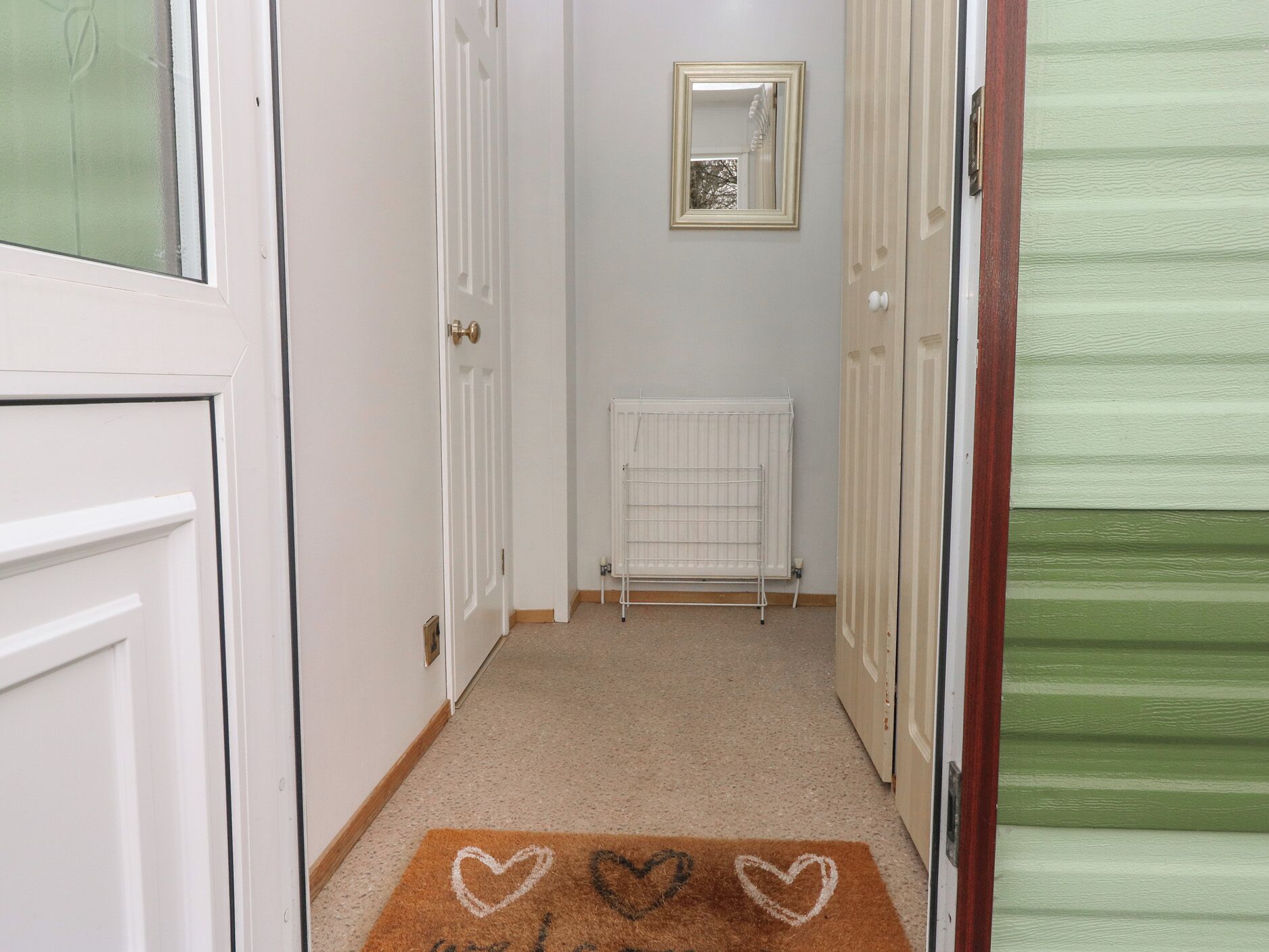A narrow hallway with white doors, a radiator, and a doormat with heart designs.
