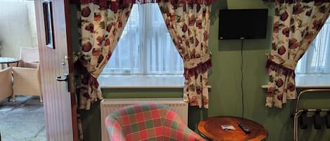 A cozy room with a plaid armchair, a small round table, and a television on the wall.