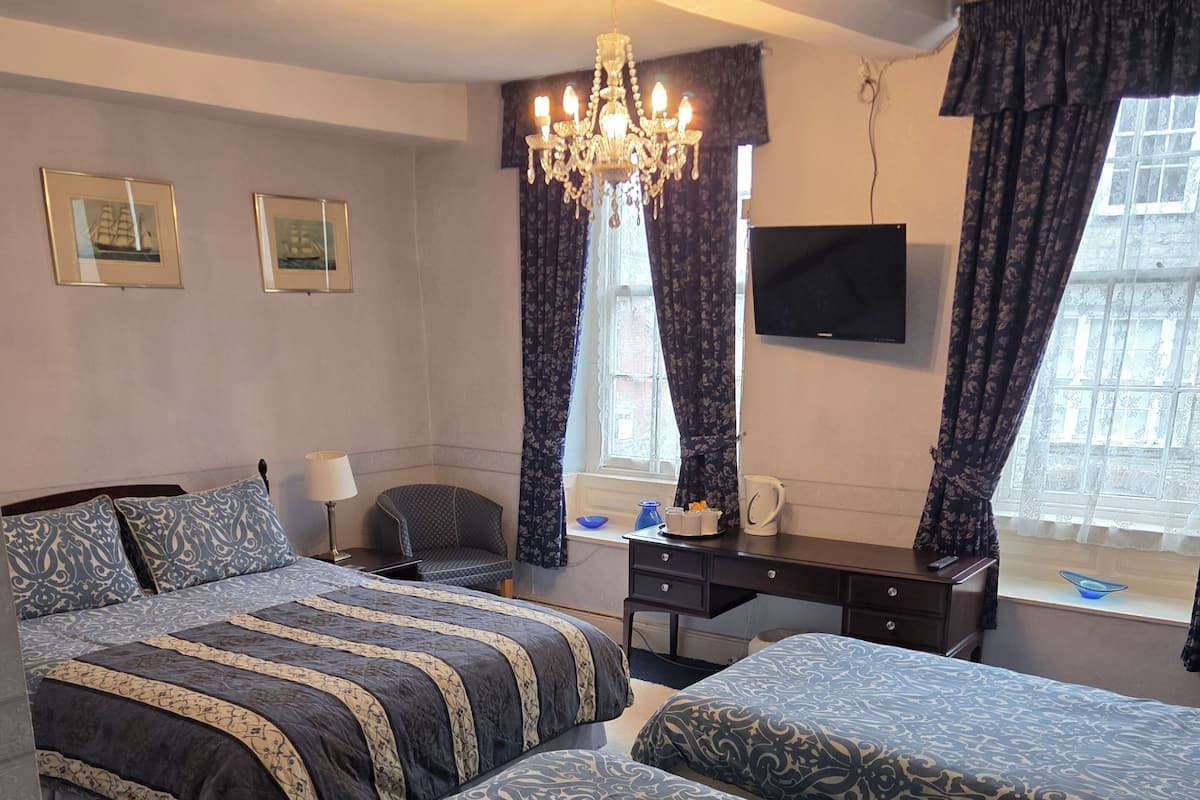 A hotel room with two beds, a desk, a chair, a television, and a chandelier.