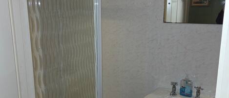 A bathroom with a glass shower enclosure, a sink with two faucets, and a mirror above the sink.