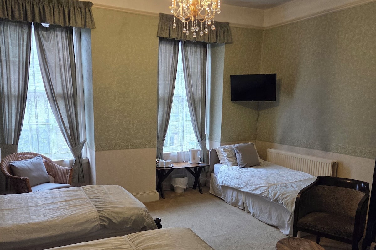 A hotel room with two beds, a chandelier, a television, and a small table.