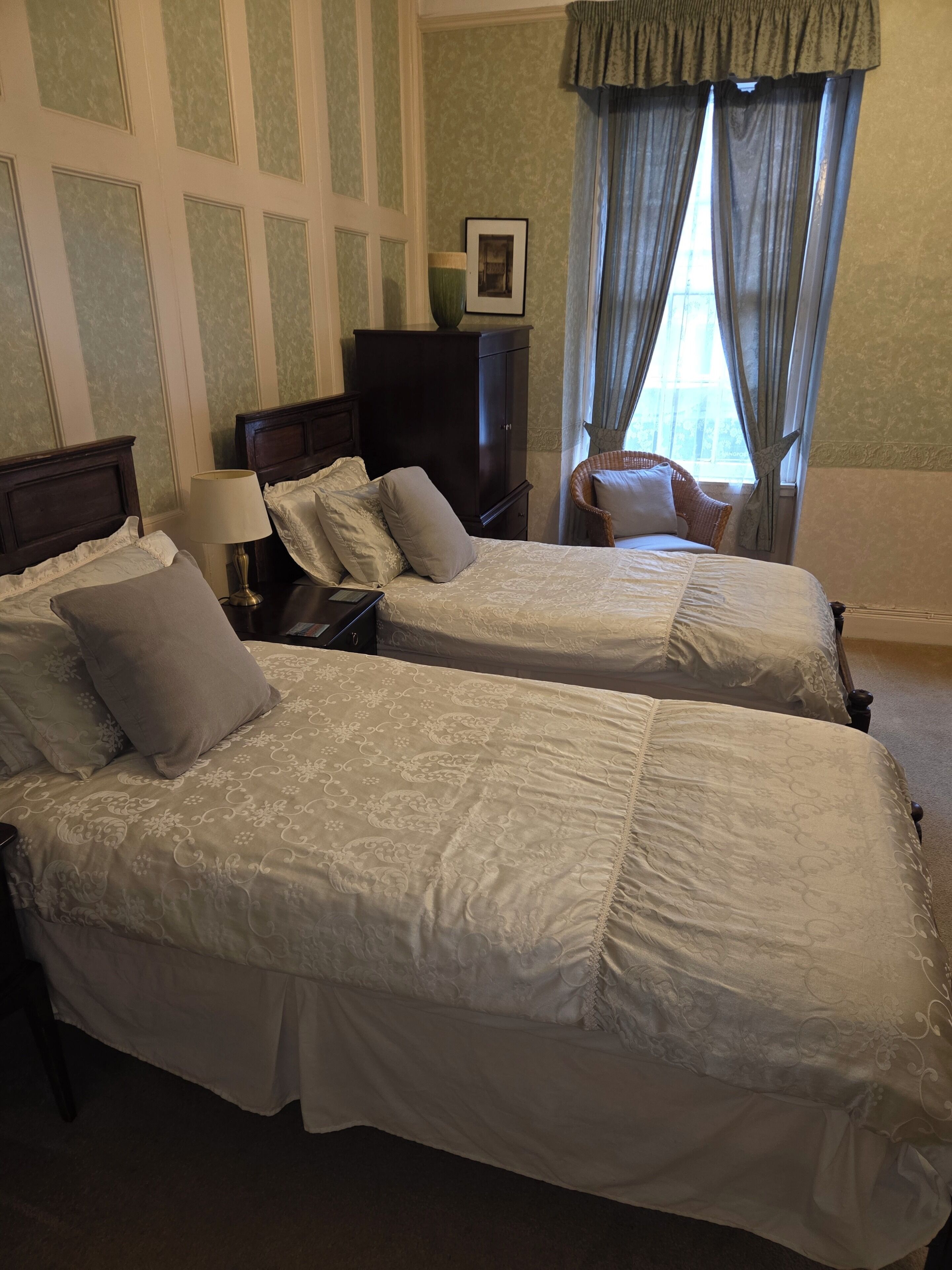 A hotel room with two beds, a nightstand, a lamp, a dresser, a chair, and a window with curtains.