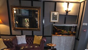 Ein gemütlicher Lounge-Bereich mit Ledersofas, einem Holztisch und gemusterten Sesseln. Große Spiegel und gerahmte Kunstwerke schmücken die Wände.