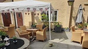 Eine Terrasse mit Korbmöbeln, einem Tisch und Kübelpflanzen.