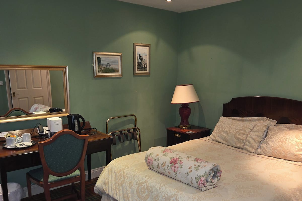 A hotel room with a bed, a desk, a chair, a lamp, and a mirror.