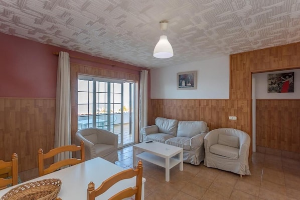 A living room with a wooden ceiling, a white table, two sofas, and a window with curtains. - Apartamentos Finca COLON (Los Quemados)