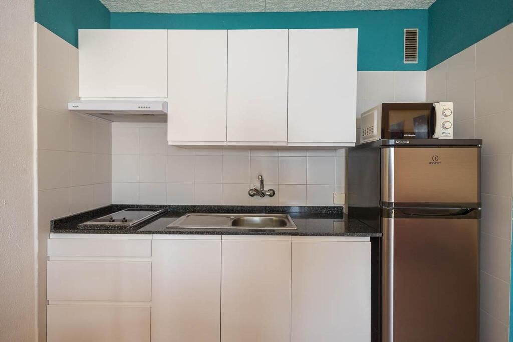 A compact kitchen with white cabinets, a stainless steel refrigerator, and a microwave on top.