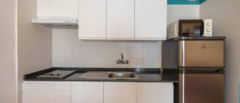 A compact kitchen with white cabinets, a stainless steel refrigerator, and a microwave on top.