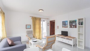 Een moderne woonkamer met een bank, stoelen, een televisie en een boekenkast.