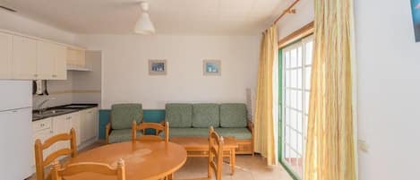 Eine kompakte Küche mit weißen Schränken, einem Esstisch mit Stühlen, einem grünen Sofa und einem großen Fenster mit Vorhängen.