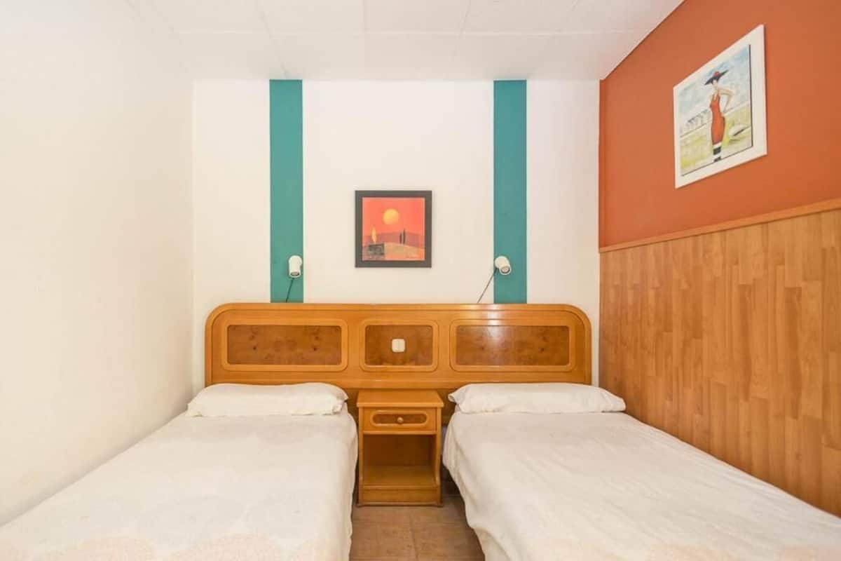 Una habitación con cabecera de madera, dos camas individuales, una mesita de noche y un cuadro en la pared.