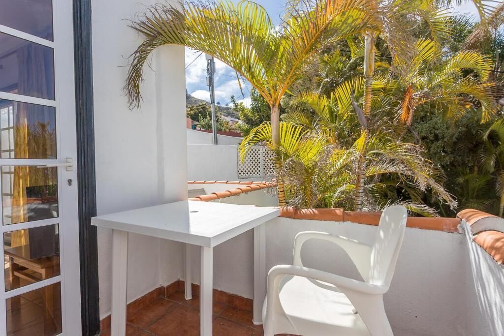 A balcony with a white table and chairs, surrounded by tropical plants.