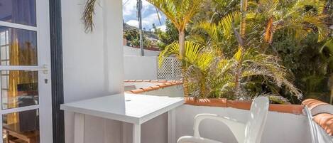 A balcony with a white table and chairs, surrounded by tropical plants.