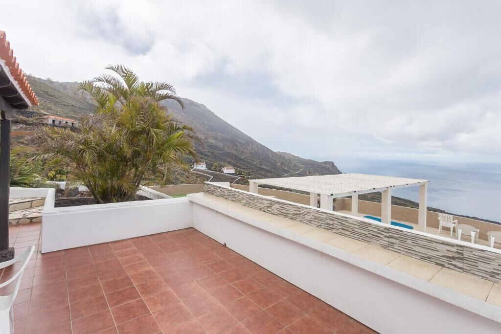 Une terrasse avec vue sur la mer, un bâtiment blanc et un palmier.