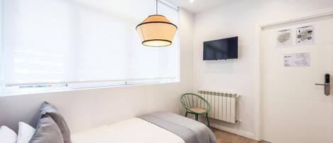 Un dormitorio con cama, lámpara colgante, radiador, televisor y puerta con cerradura.
