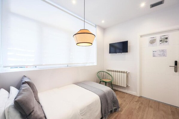 A bedroom with a bed, a hanging light fixture, a radiator, a television, and a door with a lock.