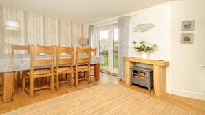 Un coin repas avec une table et des chaises en bois, une cheminée et une vue sur l’extérieur, accessible par une porte vitrée.
