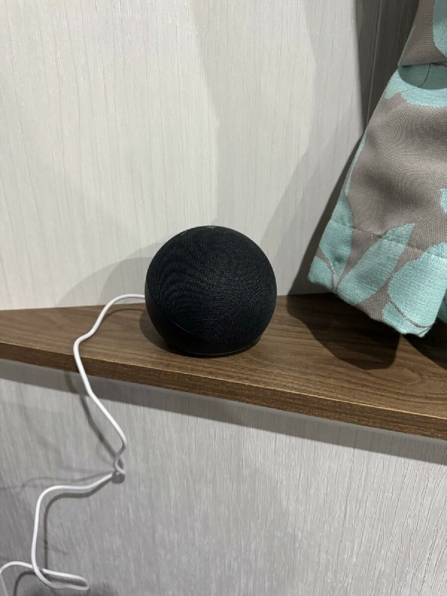 A black speaker on a wooden shelf with a white cable connected to it.