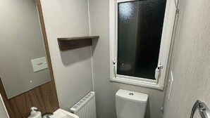 A small, compact bathroom with a white sink, a toilet, and a window. - Butlins Skegness - Holiday Accommodation 21028 (Skegness)