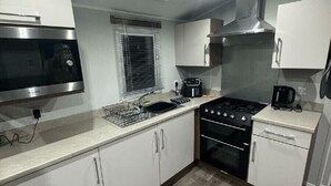 A compact kitchen with white cabinets, a stainless steel microwave, a gas stove, and a built-in oven. - Butlins Skegness - Holiday Accommodation 21028 (Skegness)