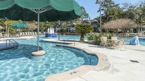 Uma área de piscina com guarda-sol verde, espreguiçadeiras e uma fonte.