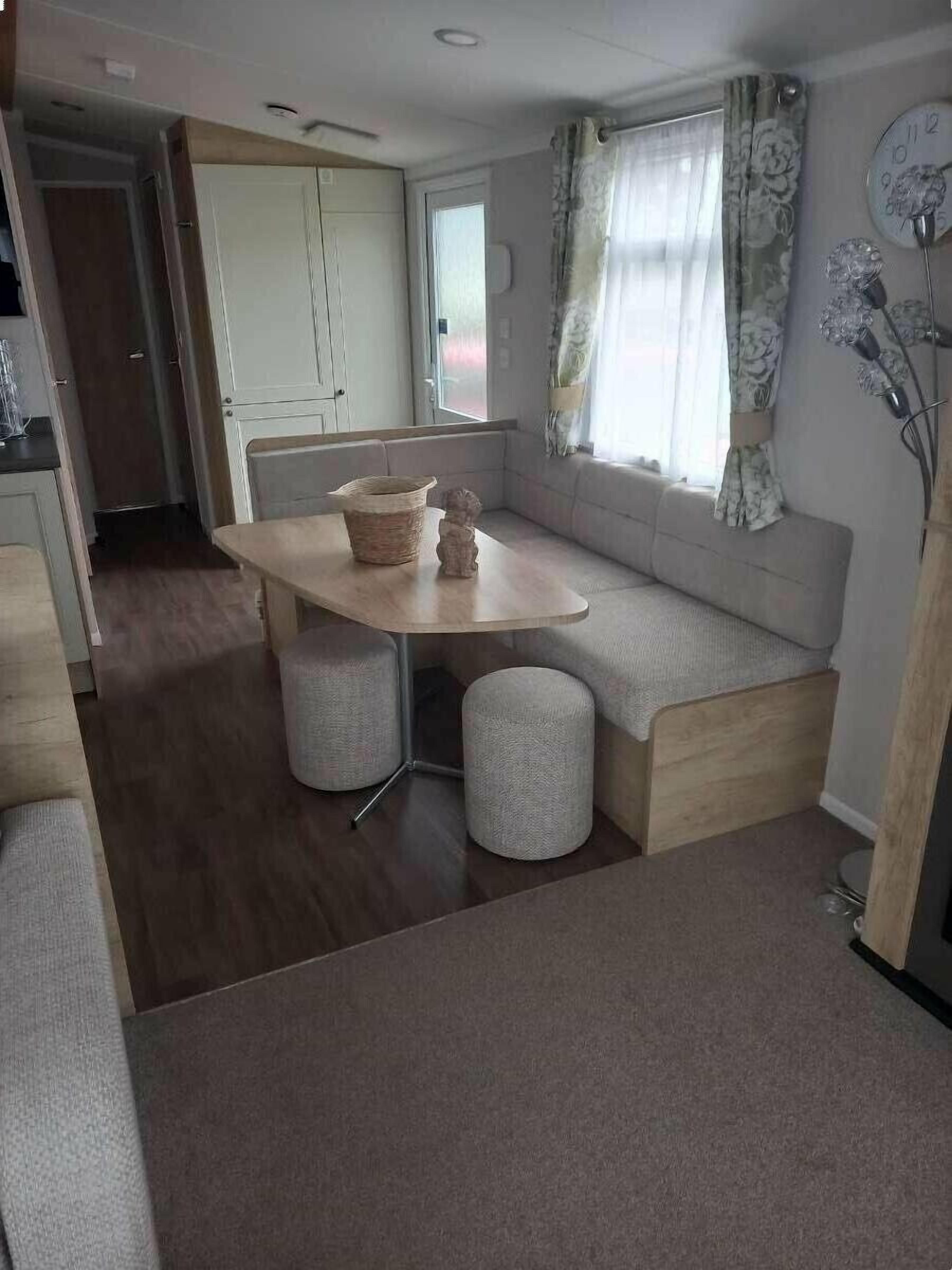 A compact living space with a kitchenette, a dining area with a table and two stools, a sofa, and a window with curtains.