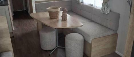 A compact living space with a kitchenette, a dining area with a table and two stools, a sofa, and a window with curtains.