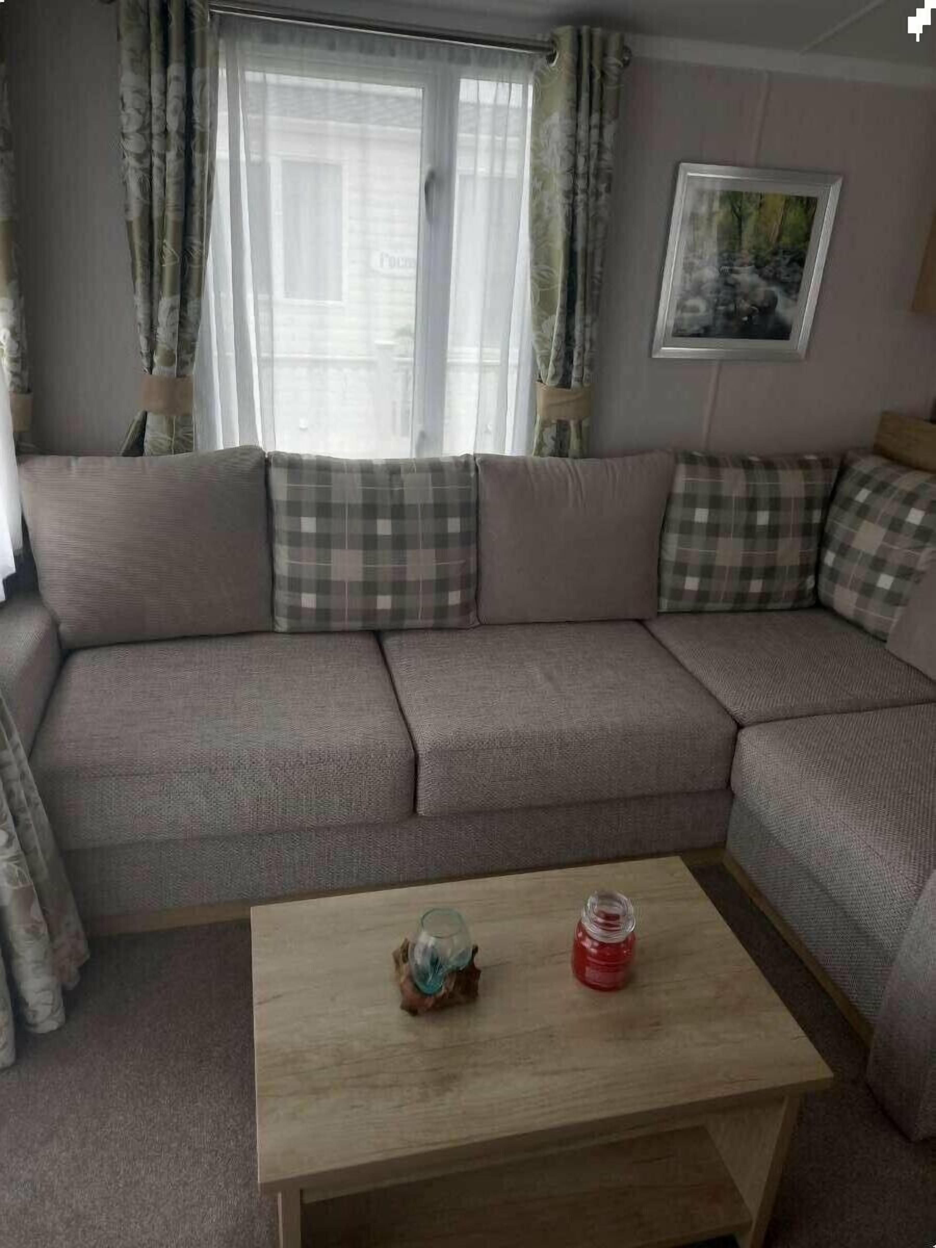 Una sala de estar con un sofá seccional, una pequeña mesa de centro de madera y un ventanal con cortinas.