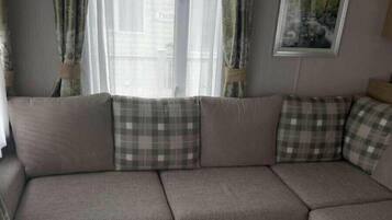 Una sala de estar con un sofá seccional, una pequeña mesa de centro de madera y un ventanal con cortinas.