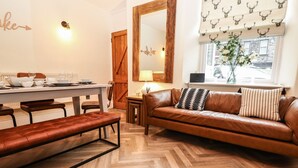 A cozy living room with a brown leather sofa, a wooden coffee table, and a herringbone-patterned floor. - Waterhead Cottage (Ambleside)