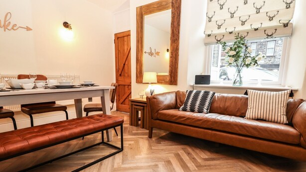 Un salon chaleureux avec un canapé en cuir marron, une table basse en bois et un parquet à motifs chevrons.