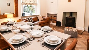 Un coin repas avec une table dressée pour quatre personnes, un canapé, une cheminée et une fenêtre agrémentée de rideaux à motifs.