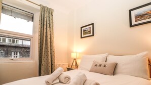 Une chambre d’hôtel avec un lit, une fenêtre avec des rideaux, une lampe et un tableau encadré au mur.