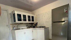 Una cocina compacta con armarios blancos, un refrigerador de acero inoxidable y una estufa a gas.