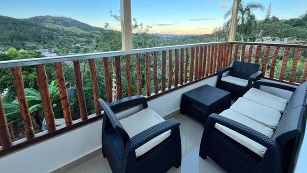 Un balcón con mobiliario de mimbre, baranda de madera y vista a un paisaje montañoso.