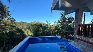 Una piscina rectangular con muelle de madera, con abundante vegetación y un cielo azul despejado de fondo.