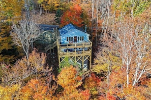 A cabin with a stone foundation and a wooden deck, surrounded by autumn foliage. - Stargazer! (Beech Mountain)