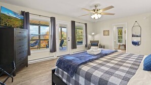 Ein Schlafzimmer mit einem großen Bett, einem Deckenventilator und Blick ins Freie durch die Fenster.