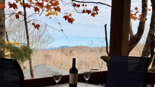 A table with a bottle of wine and two glasses, set against a backdrop of autumn leaves and a mountainous landscape. - Beech Please (Beech Mountain)