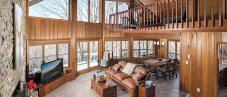 A spacious living room with a large TV, leather sofa, and a dining area with a table and chairs.