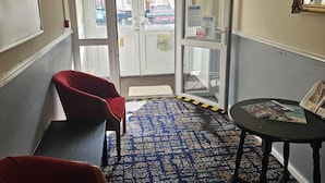 A hotel lobby with a patterned carpet, a round table with magazines, and red chairs. - Lanayr Hotel Blackpool Limited (Blackpool)