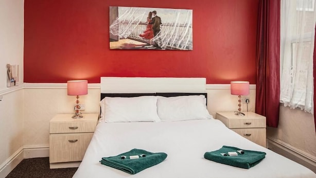 A hotel room with a red accent wall, a white bed, two bedside tables with lamps, and a painting above the bed. - Lanayr Hotel Blackpool Limited (Blackpool)