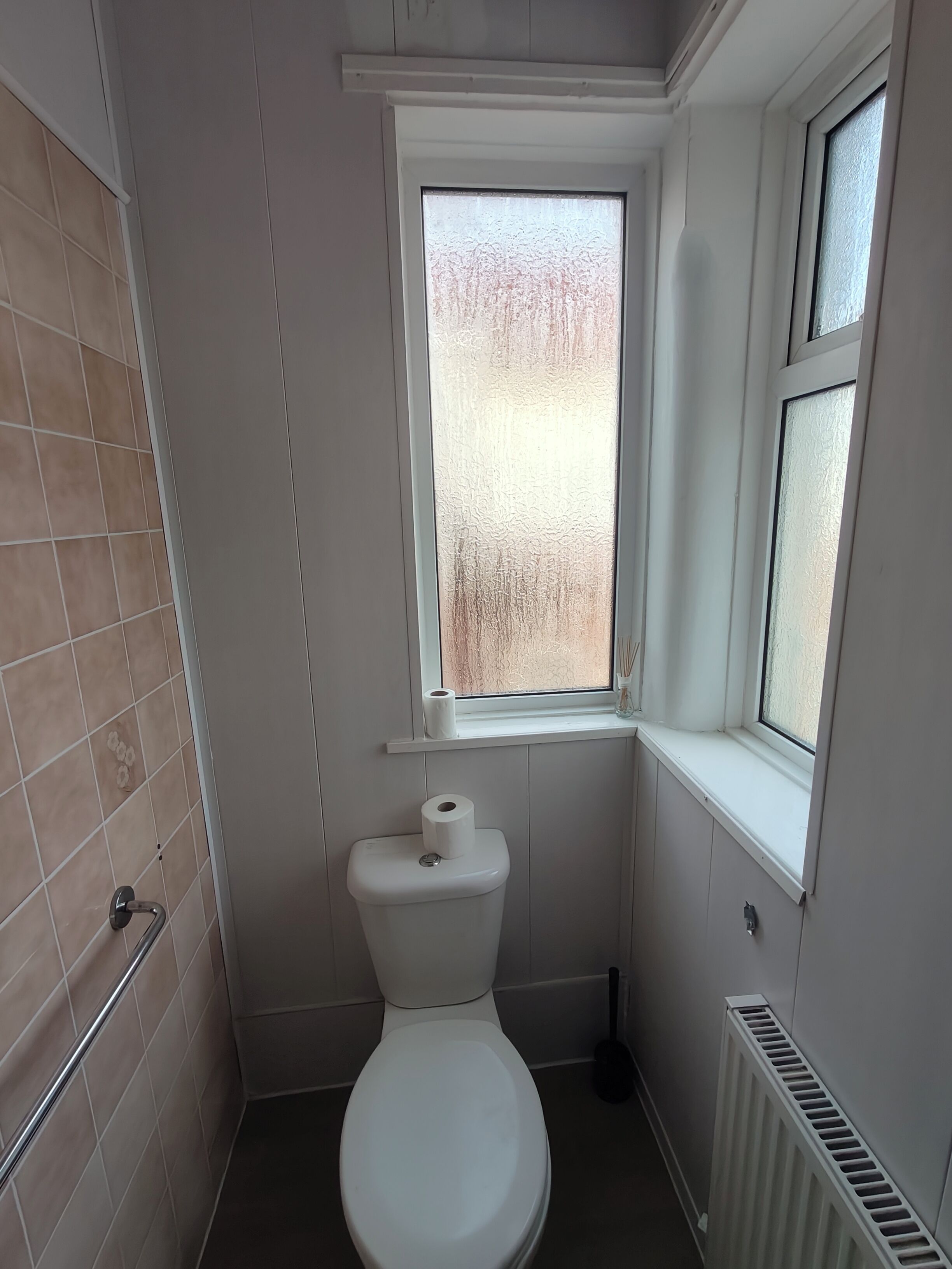 A small bathroom with a toilet, a window, and a radiator.
