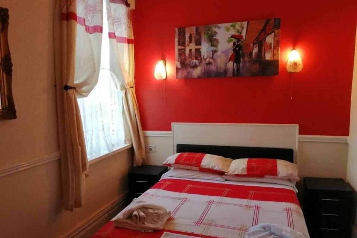 Ein Hotelzimmer mit roter Wand, einem Bett mit rotem und weißen Überwurf, einem Gemälde über dem Bett und zwei Nachttischlampen.