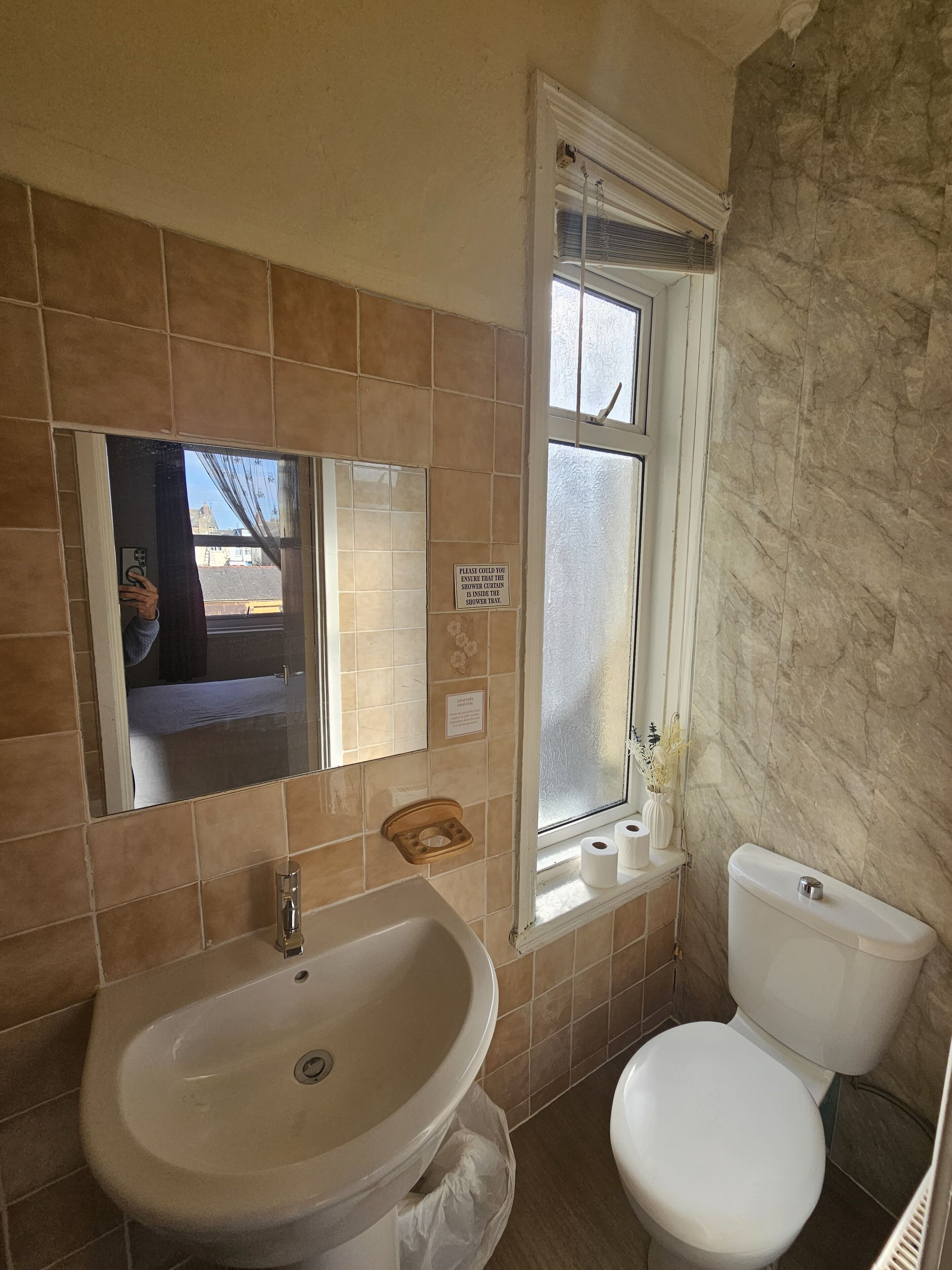 A bathroom with a sink, toilet, and a window with a shower curtain.