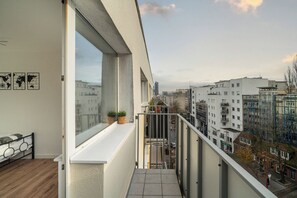 Een balkon met uitzicht op een stadsbeeld, een bed met hoofdeinde en twee bloempotten.