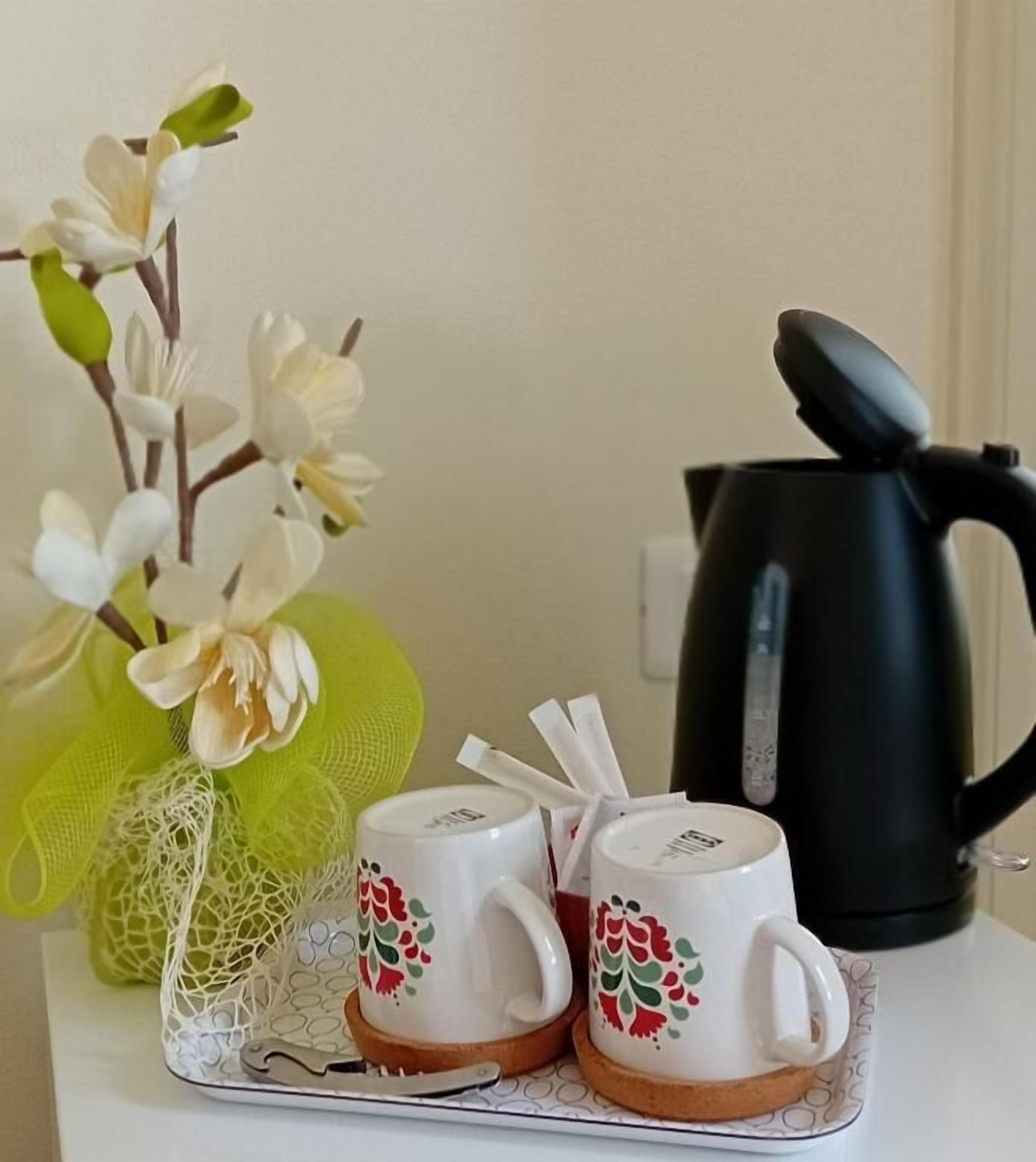A table with two white mugs with red and green floral designs, a black electric kettle, and a green decorative item.