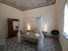 Un dormitorio con una cama con dosel, una mesita de noche con lámpara, una silla y un armario.