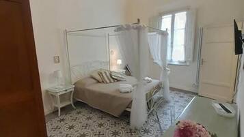 A bedroom with a canopy bed, a patterned floor, a small bedside table, and a desk with a flower.