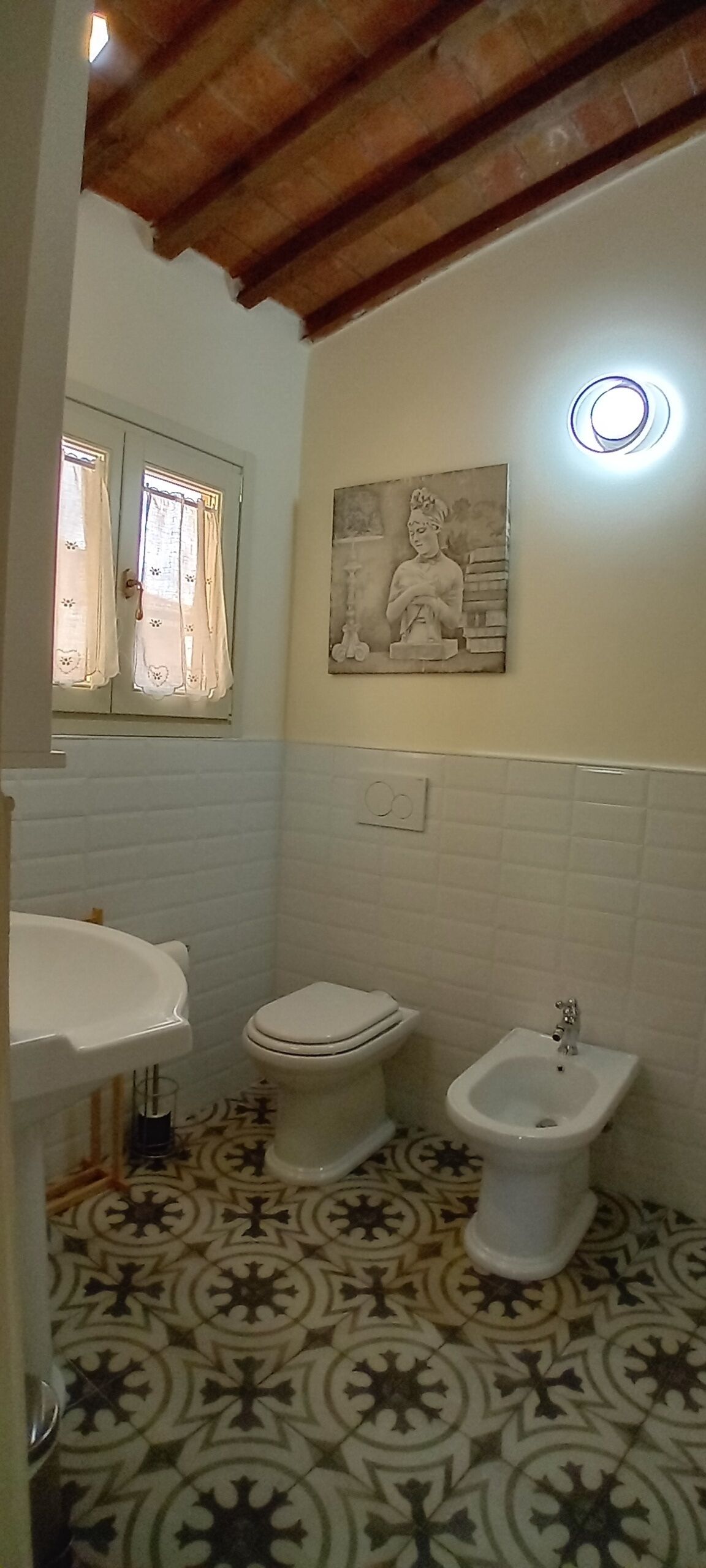 Ein Badezimmer mit Toilette, Bidet und Waschbecken, Fliesenboden und einer wandmontierten Leuchte.